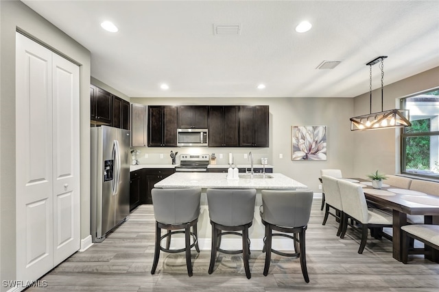 kitchen featuring an island with sink, stainless steel appliances, decorative light fixtures, and light hardwood / wood-style floors