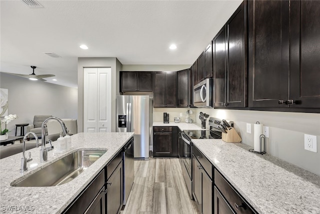 kitchen with ceiling fan, sink, stainless steel appliances, light stone counters, and light hardwood / wood-style floors