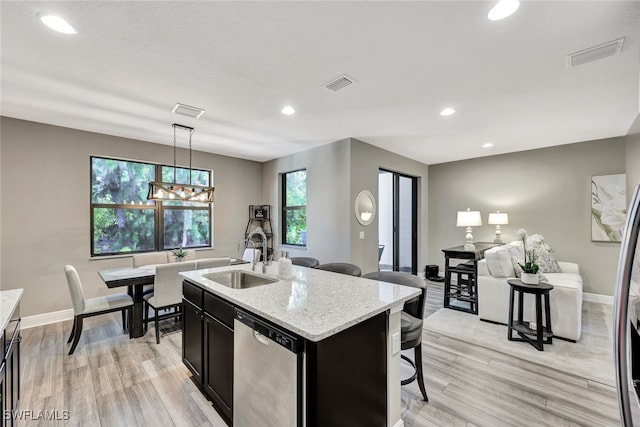 kitchen featuring pendant lighting, sink, stainless steel dishwasher, an island with sink, and light stone counters