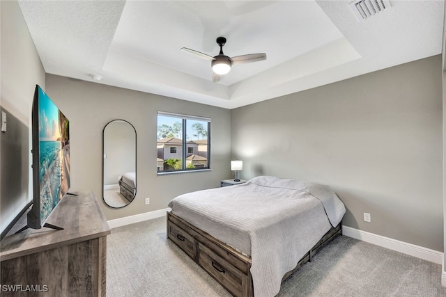 carpeted bedroom with a textured ceiling, a tray ceiling, and ceiling fan