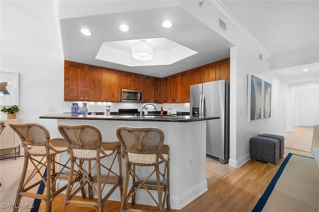 kitchen featuring a breakfast bar, appliances with stainless steel finishes, light hardwood / wood-style floors, and ornamental molding