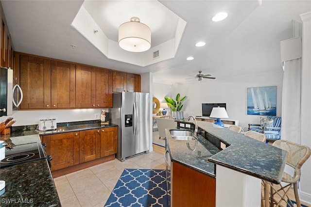 kitchen with sink, light tile patterned floors, appliances with stainless steel finishes, a tray ceiling, and a kitchen island