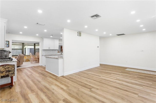 kitchen featuring white cabinetry, light stone counters, decorative backsplash, and light hardwood / wood-style flooring