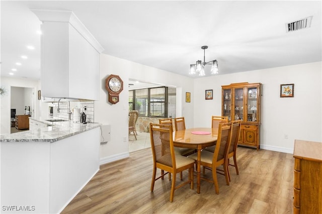 dining room with sink, a chandelier, and light hardwood / wood-style floors