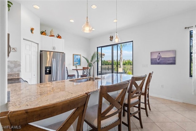 kitchen featuring kitchen peninsula, stainless steel fridge, sink, pendant lighting, and white cabinetry