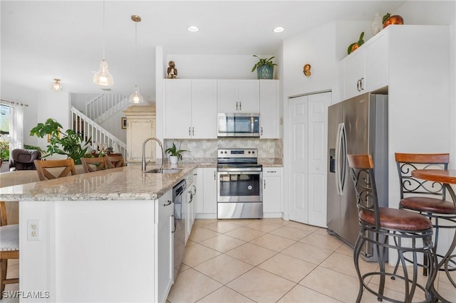 kitchen with white cabinets, sink, hanging light fixtures, light stone counters, and stainless steel appliances