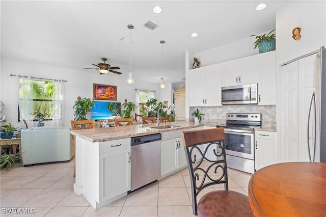 kitchen with light stone countertops, appliances with stainless steel finishes, sink, decorative light fixtures, and white cabinets