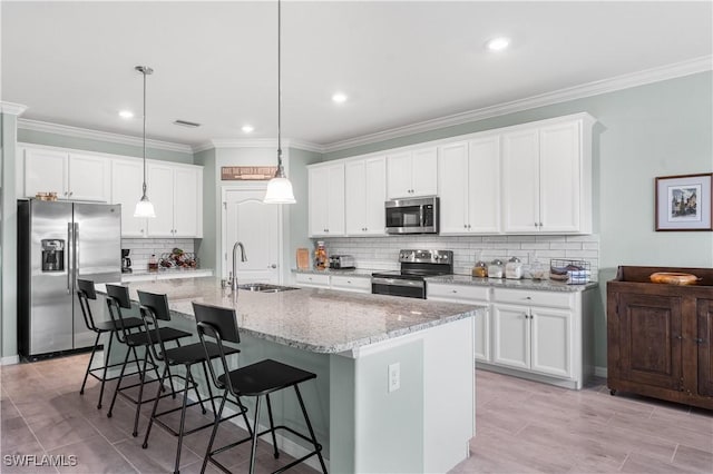 kitchen featuring appliances with stainless steel finishes, a kitchen island with sink, sink, white cabinets, and hanging light fixtures