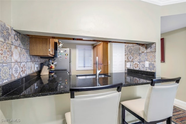 kitchen featuring a peninsula, freestanding refrigerator, a sink, brown cabinets, and backsplash