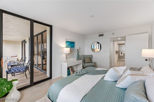 bedroom featuring multiple windows, access to exterior, light hardwood / wood-style floors, and floor to ceiling windows