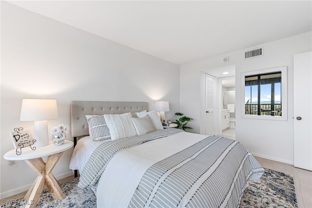 bedroom featuring visible vents, baseboards, ensuite bath, and wood finished floors