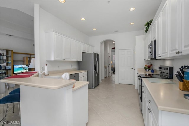 kitchen with a kitchen breakfast bar, light tile patterned flooring, kitchen peninsula, white cabinets, and appliances with stainless steel finishes