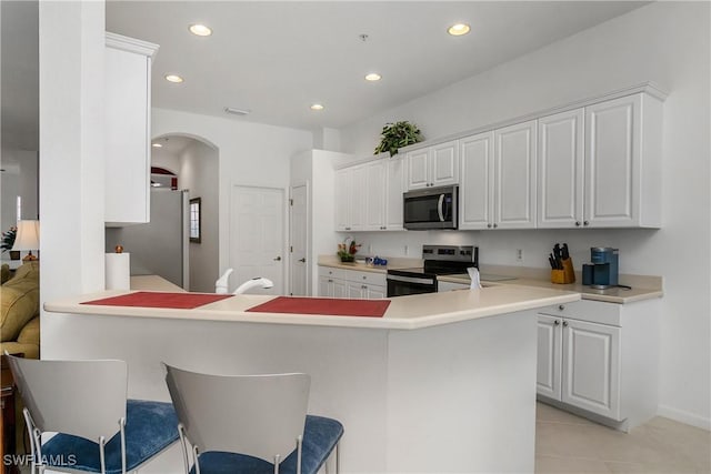 kitchen featuring light tile patterned floors, kitchen peninsula, a breakfast bar, white cabinets, and appliances with stainless steel finishes