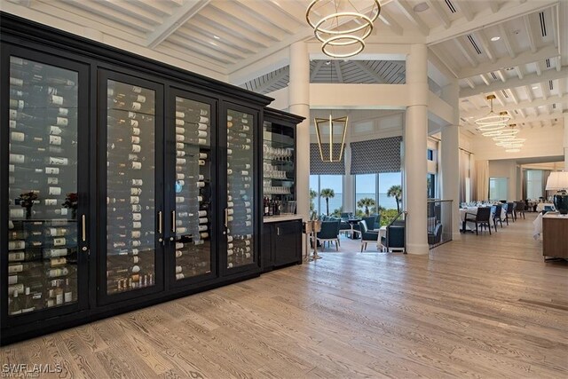 wine area with beamed ceiling, hardwood / wood-style floors, bar, and a notable chandelier