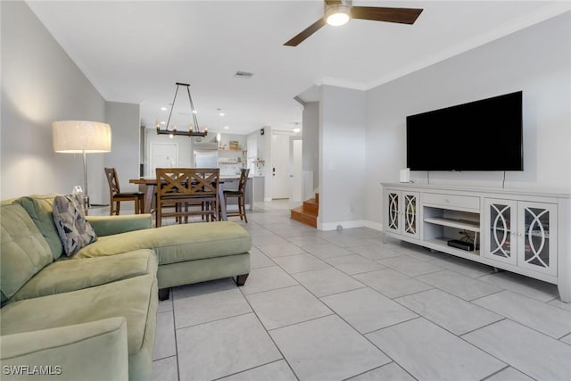 living room with crown molding, ceiling fan with notable chandelier, visible vents, baseboards, and stairs