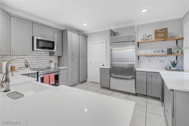 kitchen featuring light stone counters, built in appliances, light tile patterned floors, and gray cabinetry