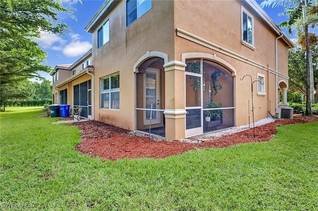 rear view of house with a yard, central AC, a sunroom, and stucco siding