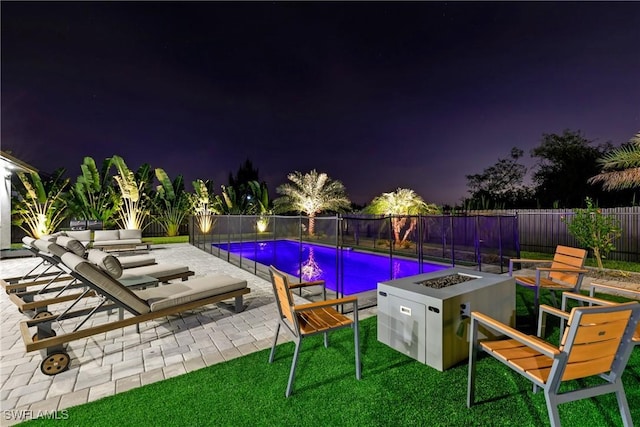 pool at night featuring a yard, a patio, and a fire pit