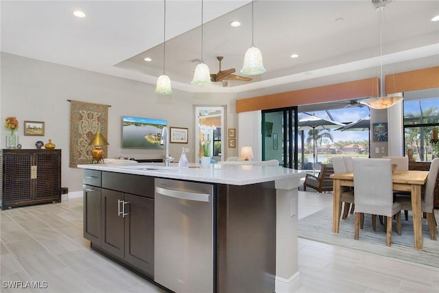 kitchen with dishwasher, an island with sink, decorative light fixtures, and a tray ceiling