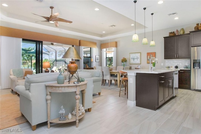 kitchen featuring pendant lighting, decorative backsplash, an island with sink, a tray ceiling, and stainless steel appliances