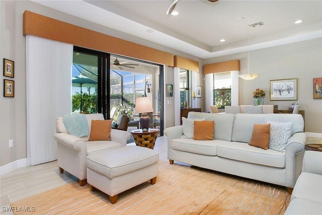 living room featuring a raised ceiling, ceiling fan, and light hardwood / wood-style flooring