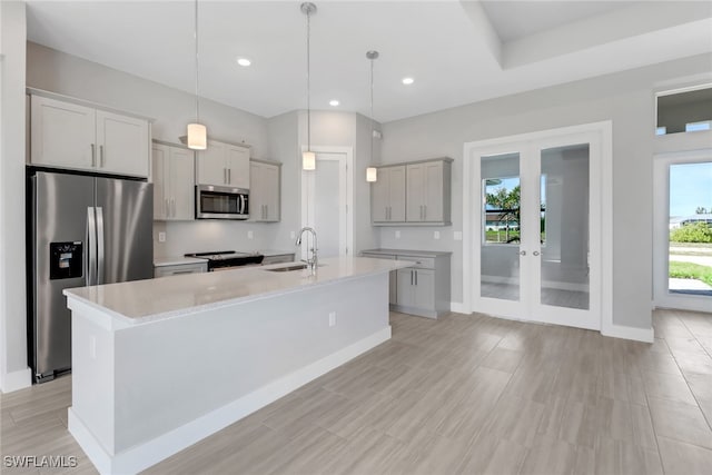 kitchen featuring hanging light fixtures, stainless steel appliances, a center island with sink, and sink