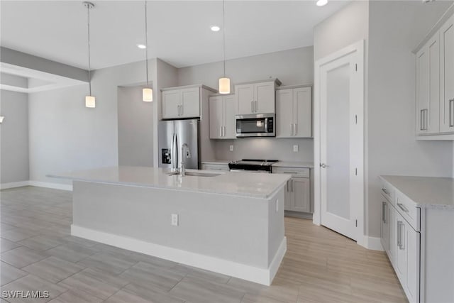 kitchen featuring light stone counters, stainless steel appliances, sink, pendant lighting, and a center island with sink