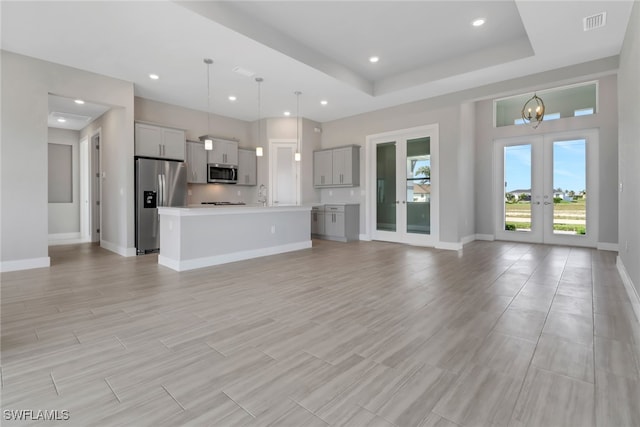 unfurnished living room with french doors, a tray ceiling, sink, light hardwood / wood-style flooring, and a chandelier