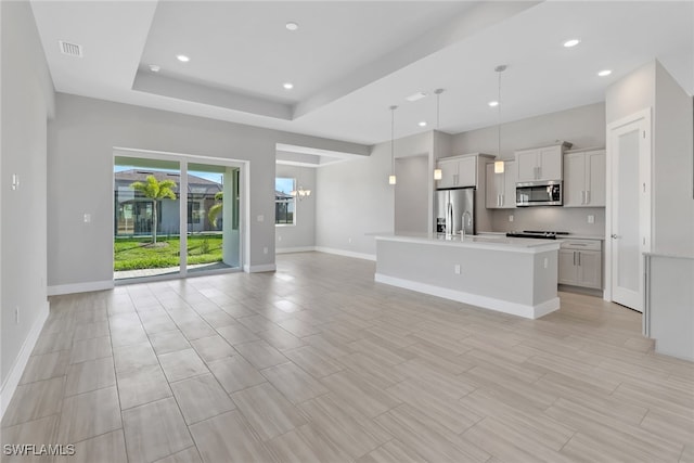 kitchen featuring hanging light fixtures, a raised ceiling, a chandelier, a kitchen island with sink, and appliances with stainless steel finishes