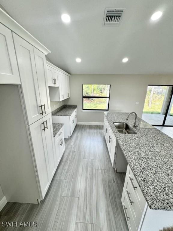 kitchen featuring stone countertops, white cabinetry, sink, and light hardwood / wood-style flooring