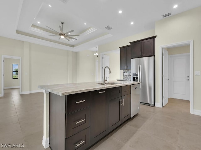 kitchen with stainless steel appliances, a raised ceiling, a center island with sink, and sink