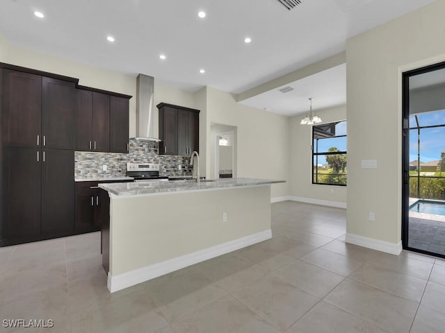 kitchen with decorative backsplash, electric range, an island with sink, and wall chimney range hood