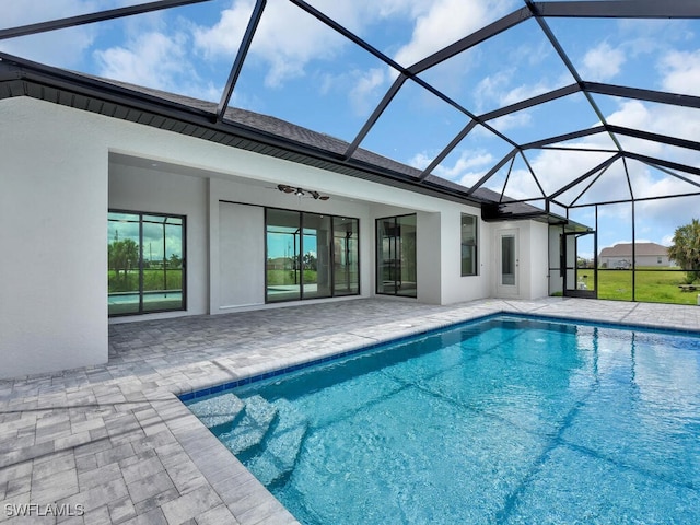 view of swimming pool with glass enclosure, ceiling fan, and a patio area