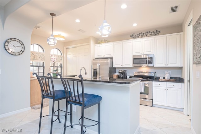 kitchen with a kitchen island with sink, white cabinets, stainless steel appliances, and light tile patterned floors