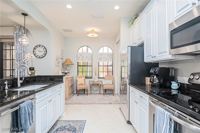 kitchen with stainless steel appliances, white cabinetry, dark stone counters, and sink