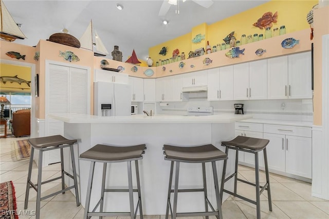 kitchen featuring a kitchen breakfast bar, white cabinetry, light tile patterned flooring, and white appliances