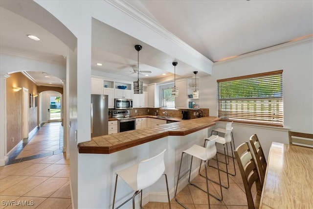 kitchen with a kitchen breakfast bar, kitchen peninsula, appliances with stainless steel finishes, decorative light fixtures, and white cabinetry