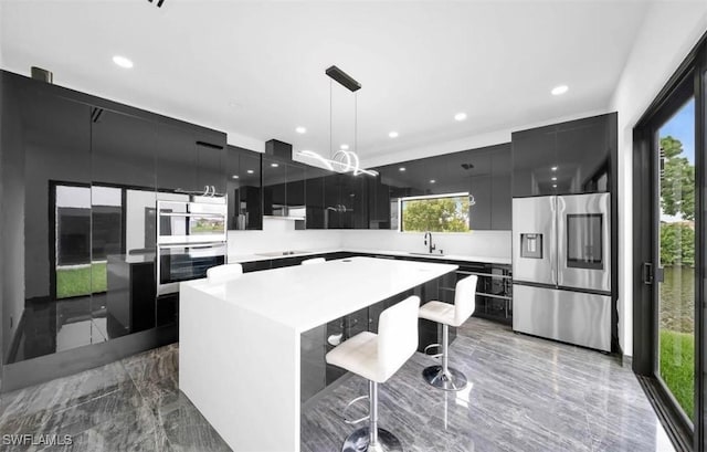 kitchen with a kitchen bar, stainless steel appliances, a healthy amount of sunlight, decorative light fixtures, and a center island