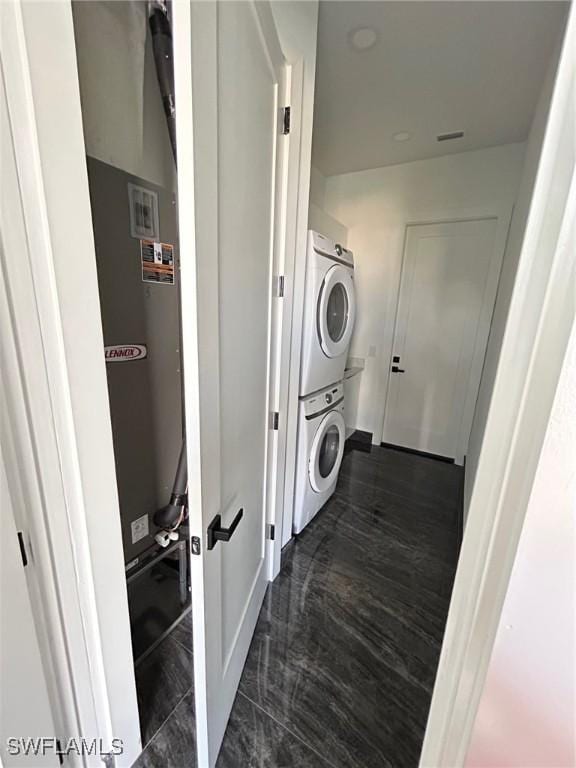 laundry room featuring stacked washer / dryer and dark tile patterned floors