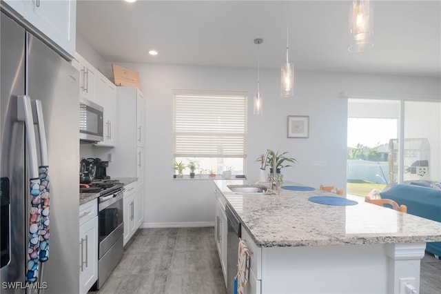 kitchen with white cabinets, sink, hanging light fixtures, an island with sink, and stainless steel appliances