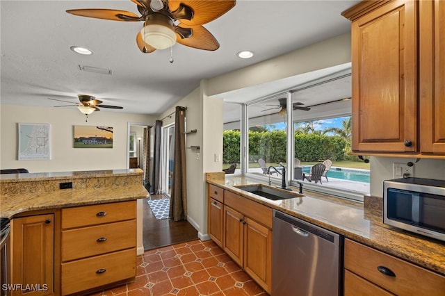 kitchen featuring light stone countertops, recessed lighting, stainless steel appliances, a sink, and brown cabinets