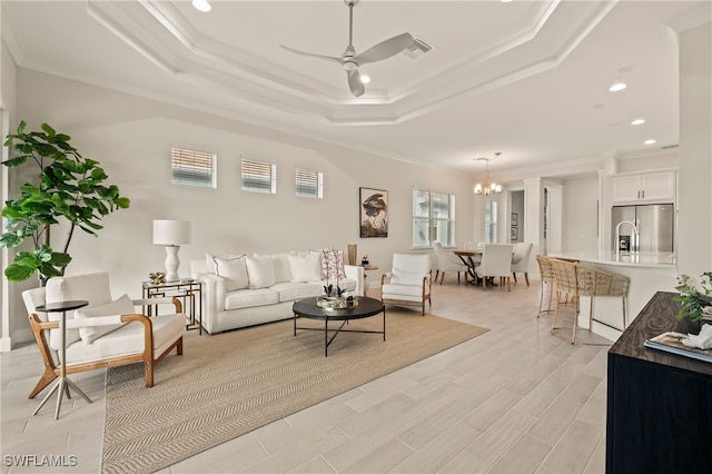 living room with ceiling fan with notable chandelier, light hardwood / wood-style floors, a raised ceiling, and crown molding