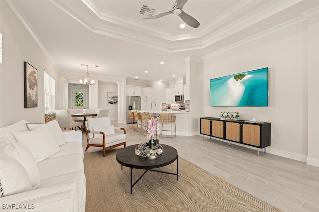 living room featuring light wood-type flooring, ornamental molding, ceiling fan with notable chandelier, a raised ceiling, and sink