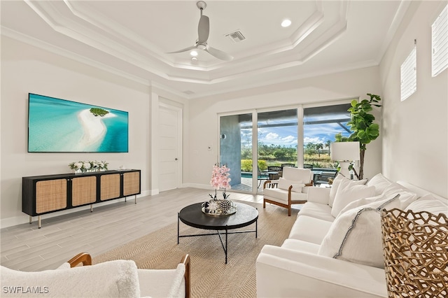 living room with ceiling fan, light hardwood / wood-style floors, a raised ceiling, and ornamental molding