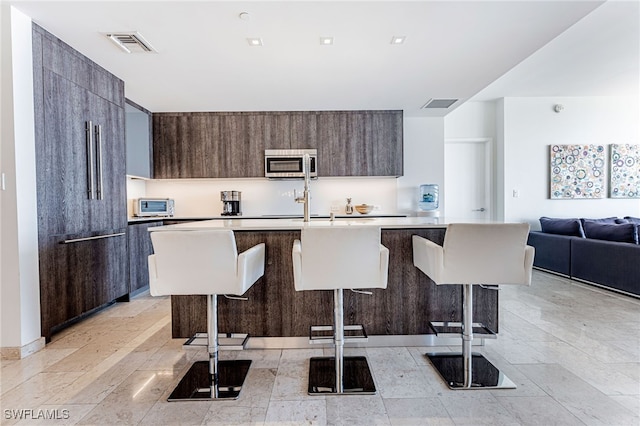 kitchen featuring a kitchen bar, paneled refrigerator, and an island with sink