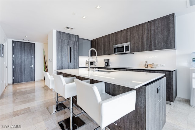 kitchen featuring a kitchen breakfast bar, a kitchen island with sink, dark brown cabinets, and sink