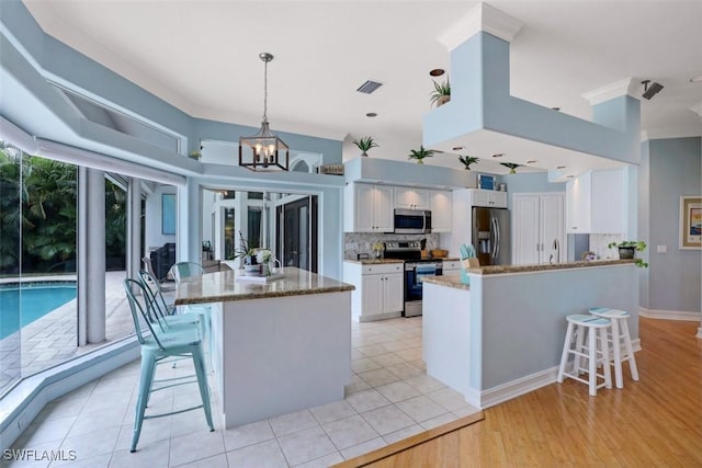 kitchen with pendant lighting, a kitchen breakfast bar, white cabinetry, and appliances with stainless steel finishes