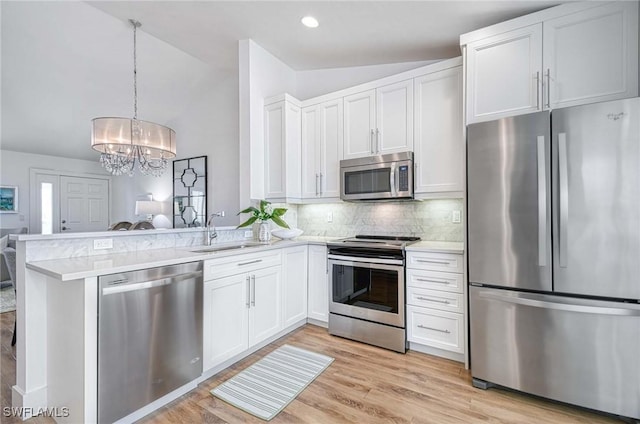 kitchen featuring stainless steel appliances, sink, white cabinetry, lofted ceiling, and kitchen peninsula