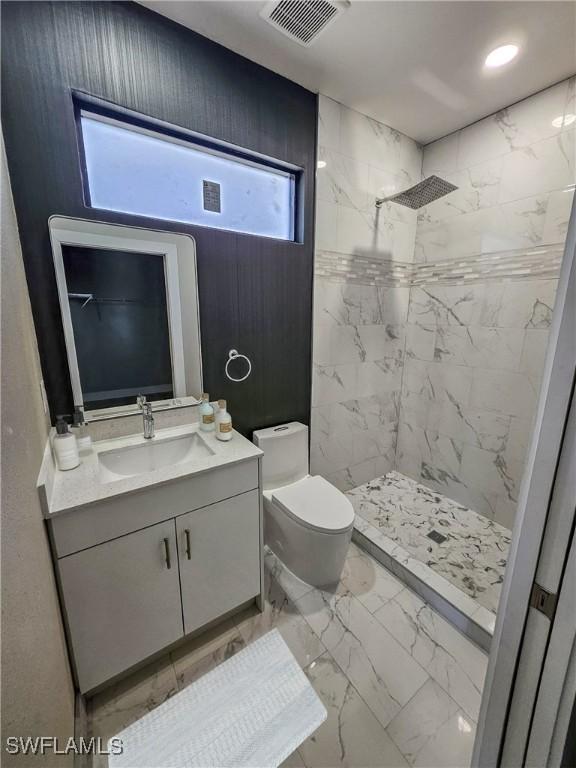 bathroom with toilet, vanity, and tiled shower