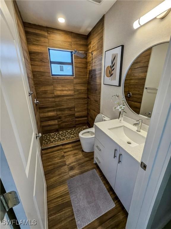 bathroom with tiled shower, hardwood / wood-style floors, vanity, and toilet